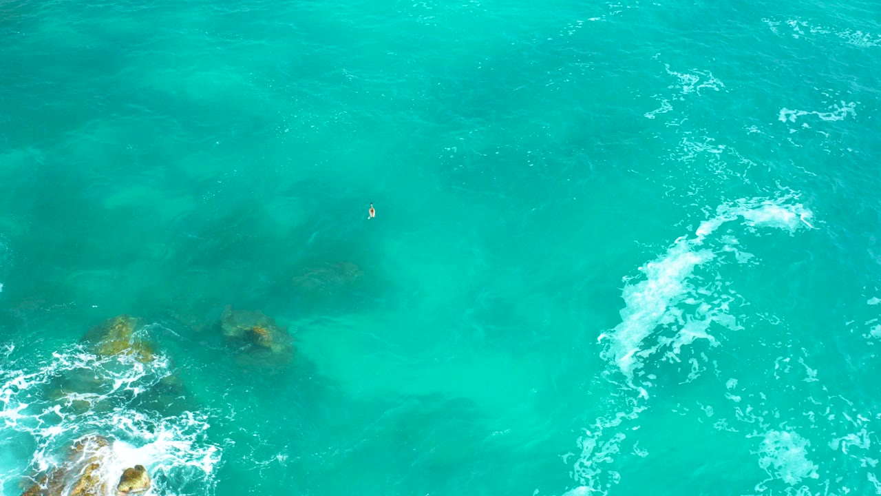 Overhead turquoise ocean with white foam and rocks near the lower left