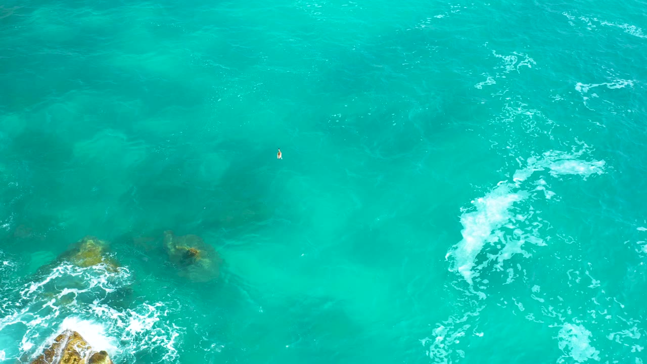 Bird's-eye view of aquamarine ocean at Secrets Marquis Los Cabos, Mexico, with surf breaking around darker submerged rocks and no visible people.