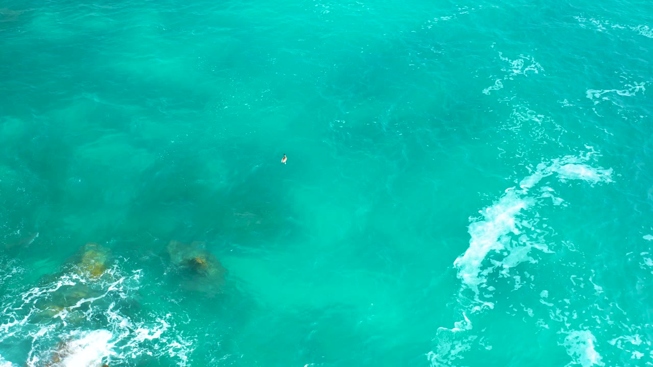 Overhead Mexican coastal water with open turquoise surface, faint underwater rock shapes, and a white foam streak along the right side, no visible people.