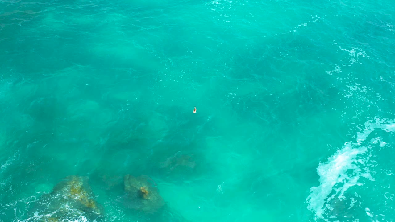 Shallow green ocean with underwater rocks and foam moving across frame.