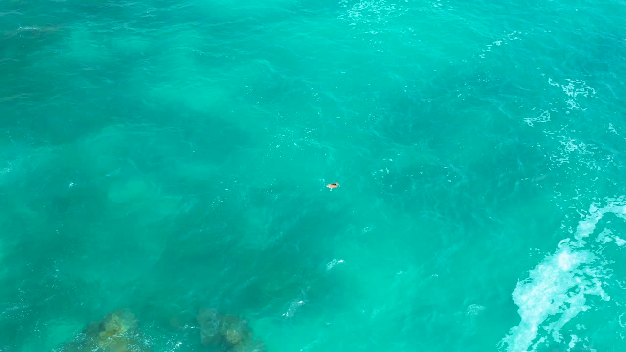 Aerial frame over green ocean water near Secrets Marquis Los Cabos, with darker underwater patches, small white foam near the lower right, and no visible people.