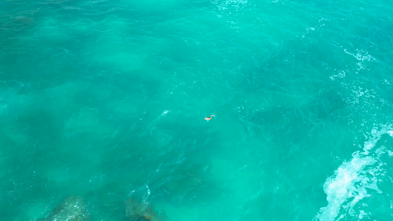 High aerial view of turquoise water near Secrets Marquis Los Cabos, with submerged rock tones near the bottom, wave foam on the right side, and no visible people.