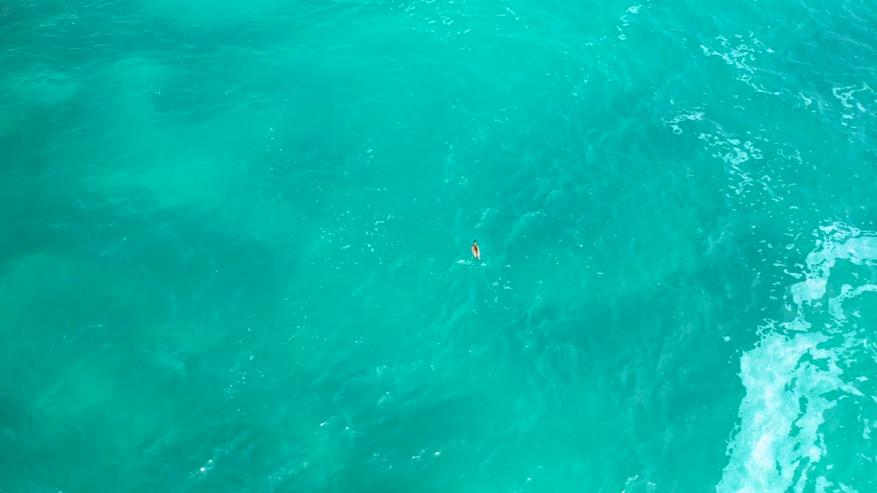 Turquoise ocean water from above with a tiny boat near the upper center.