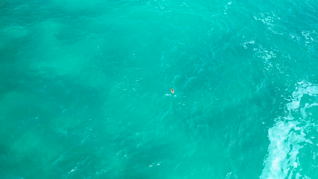 Aerial frame over blue-green water in Secrets Marquis Los Cabos, Mexico, with the small boat slightly right of center, a bright wave streak on the right edge, and no visible people.