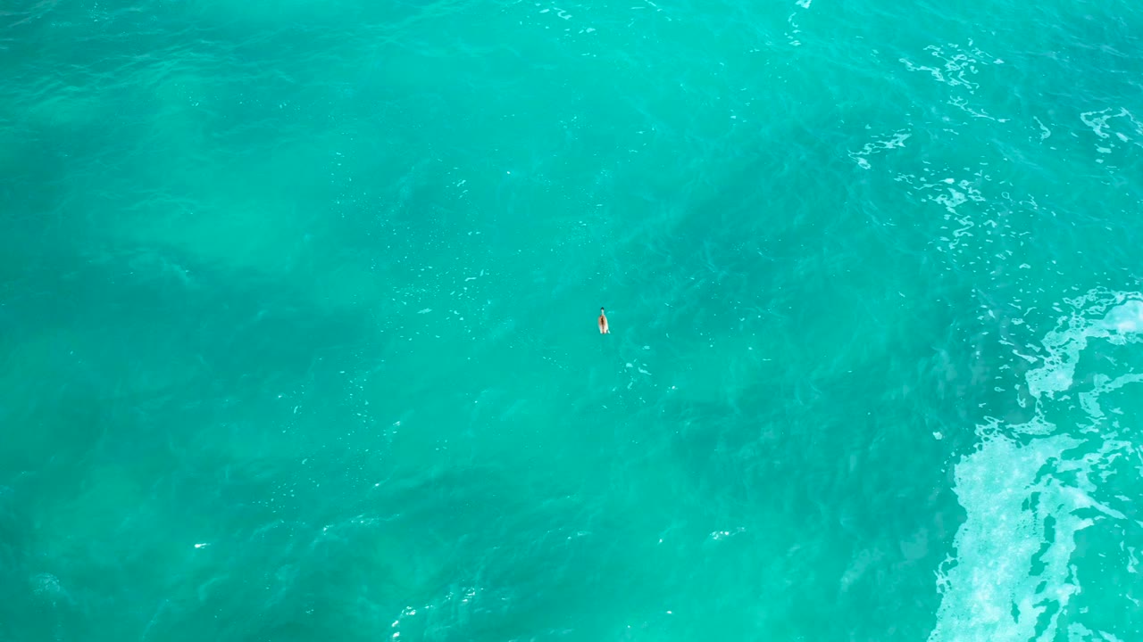 Top-down view of turquoise ocean at Secrets Marquis Los Cabos, Mexico, with the tiny boat near the upper middle, soft darker patches below the surface, and no visible people.