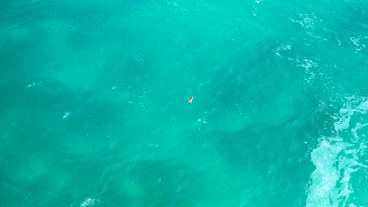 Overhead ocean view in Secrets Marquis Los Cabos, Mexico, with the tiny boat left of center, teal water gradients, pale foam on the right, and no visible people.