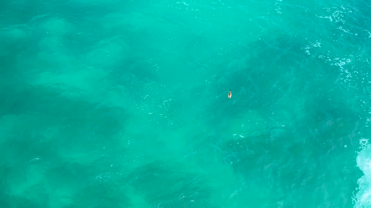 Aerial green-blue water with swimmer and breaking foam on the right