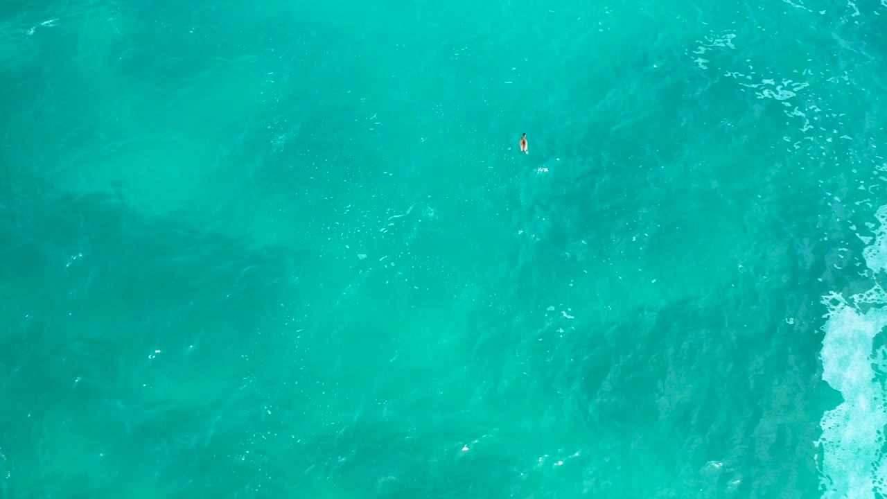Top-down view of turquoise ocean water at Secrets Marquis Los Cabos, with darker underwater patches, a small white foam streak near the right edge, and no visible people.