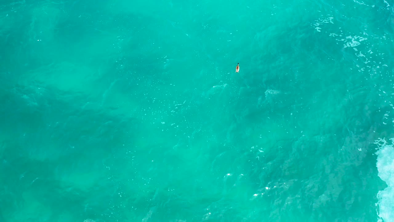 Top-down ocean frame at Secrets Marquis Los Cabos, with turquoise water, a broad darker patch below the surface, white foam entering from the right edge, and no visible people.