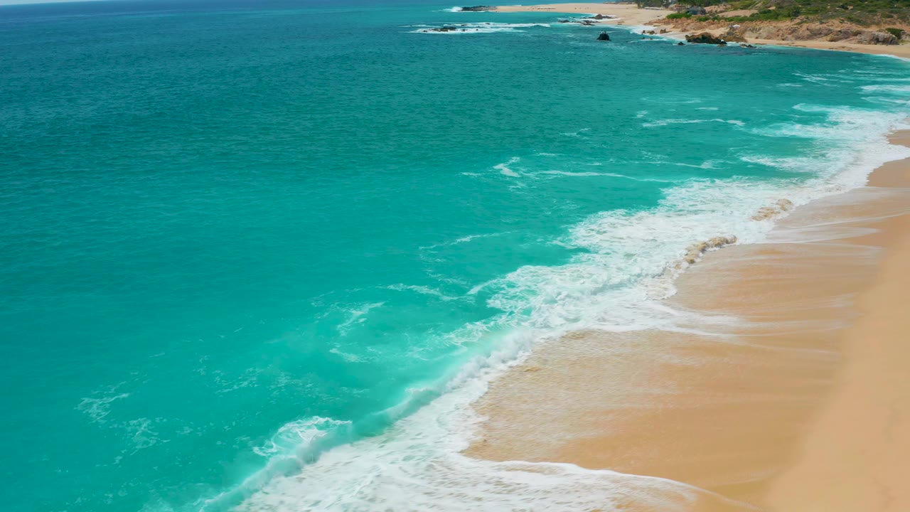 Aerial coastal frame from Secrets Marquis Los Cabos, Mexico, with blue-green water, a thinner diagonal surf line, tan beach, and no visible people.