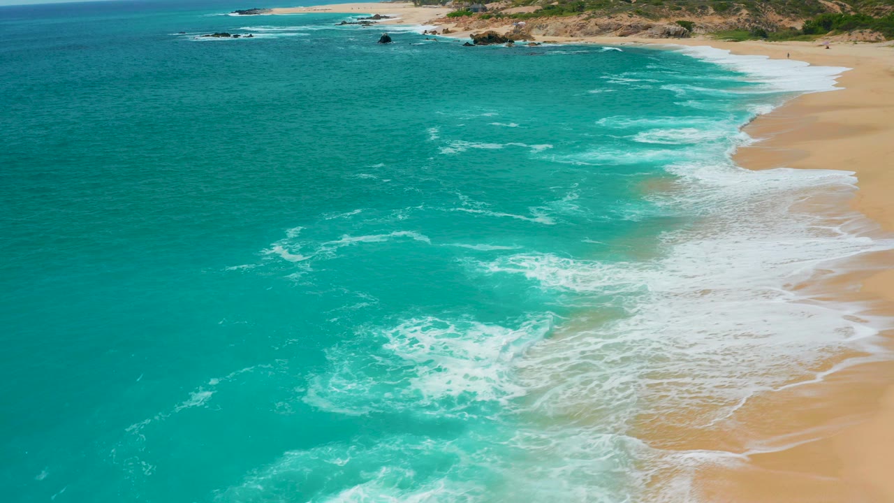 Aerial view at Secrets Marquis Los Cabos, Mexico, with turquoise water spreading white foam toward a tan beach and no visible people.