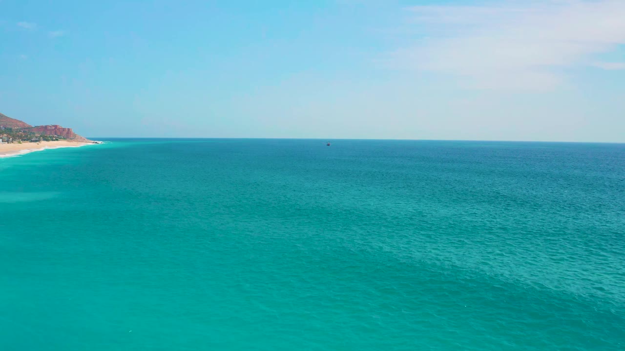 Open blue sea fills the frame near Secrets Marquis Los Cabos, Mexico, with the sandy shoreline and brown headland slightly more centered along the left edge, no visible people.