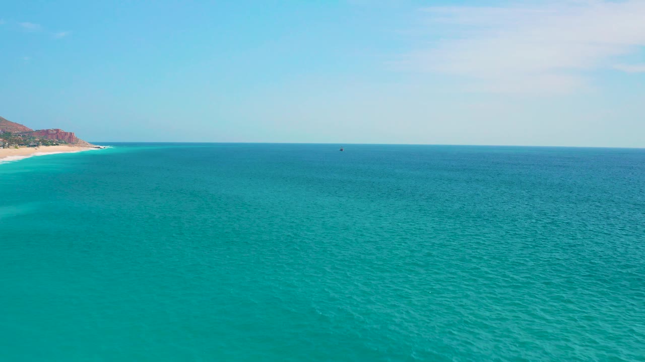A wide ocean view near Secrets Marquis Los Cabos, Mexico, shows turquoise water in the foreground and the beach and rocky-looking headland compressed to the left edge, no visible people.