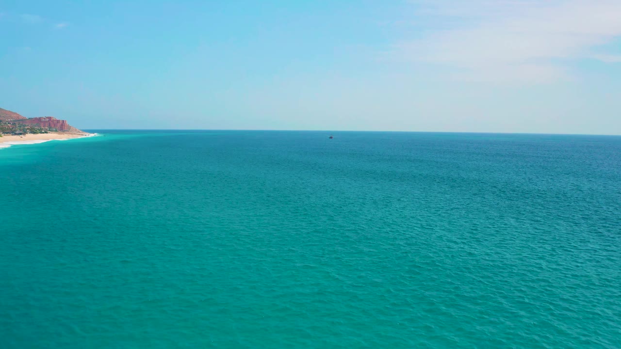 A broad blue sea view holds the horizon high in frame, with the Secrets Marquis Los Cabos shoreline still visible at the far left and no visible people.