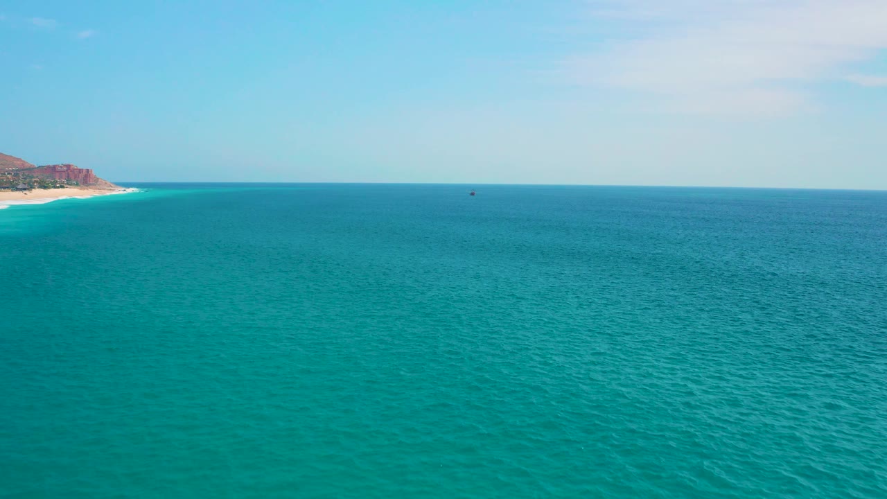 Open water fills the frame with subtle surface texture, a thin cloud patch overhead, a distant sandy coast at left, and no visible people.