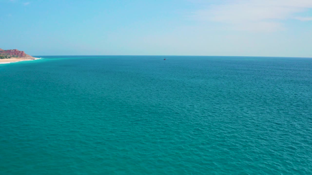 Mid-clip aerial view near Secrets Marquis Los Cabos, Mexico, showing rippled ocean water, a level horizon, light sky, and the left-edge coast, with no visible people.