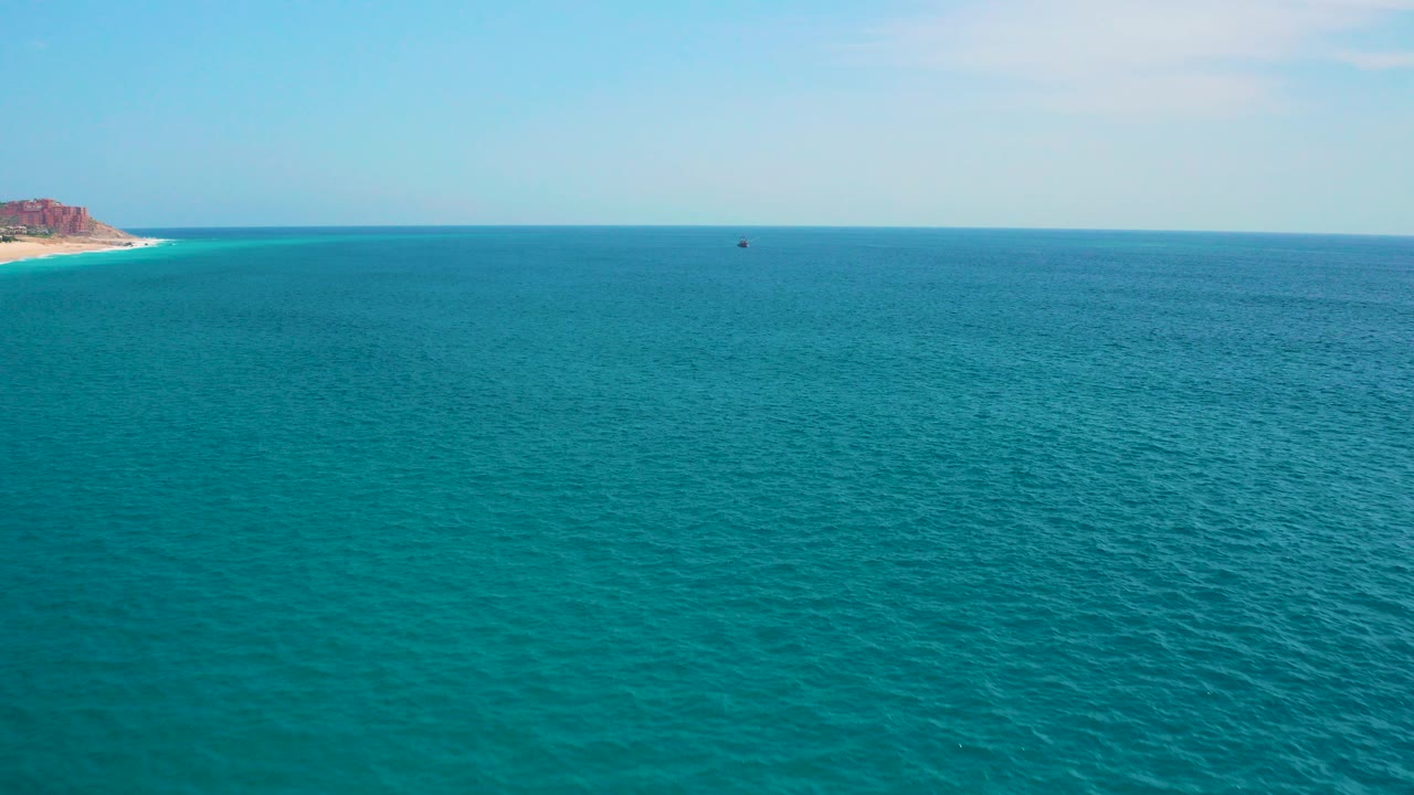 Wide elevated view of turquoise ocean near Secrets Marquis Los Cabos, Mexico, with a low horizon, rocky coast at the far left, and no visible people.