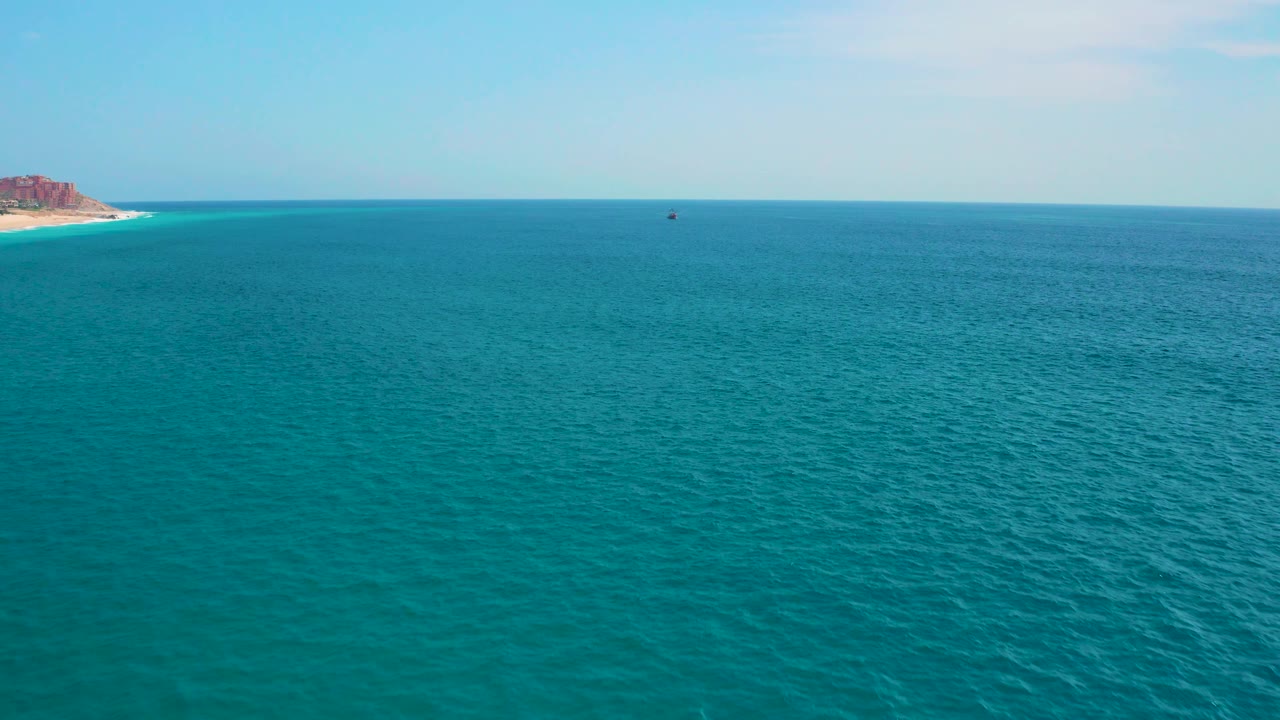 Wind-rippled turquoise water stretches toward a flat horizon near Secrets Marquis Los Cabos, Mexico, with a small coastal point at left and no visible people.