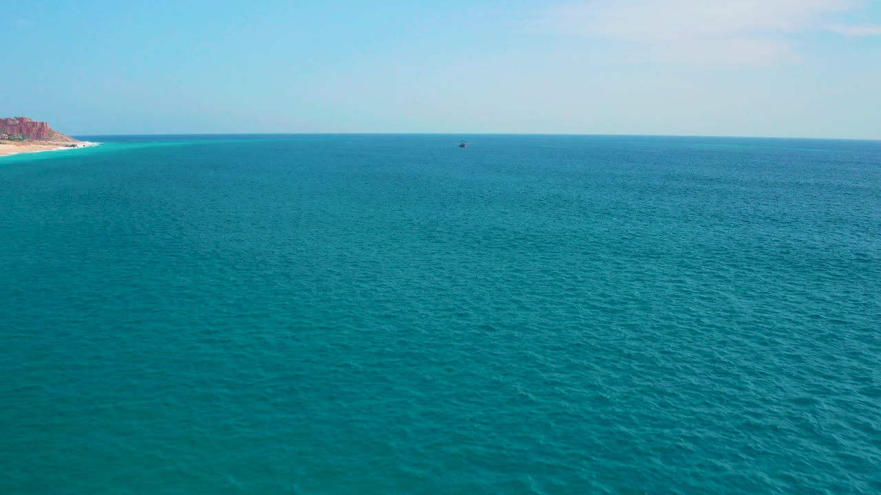 A calm expanse of sea near Secrets Marquis Los Cabos, Mexico, sits below a bright sky, with the coastline clipped along the far left and no visible people.