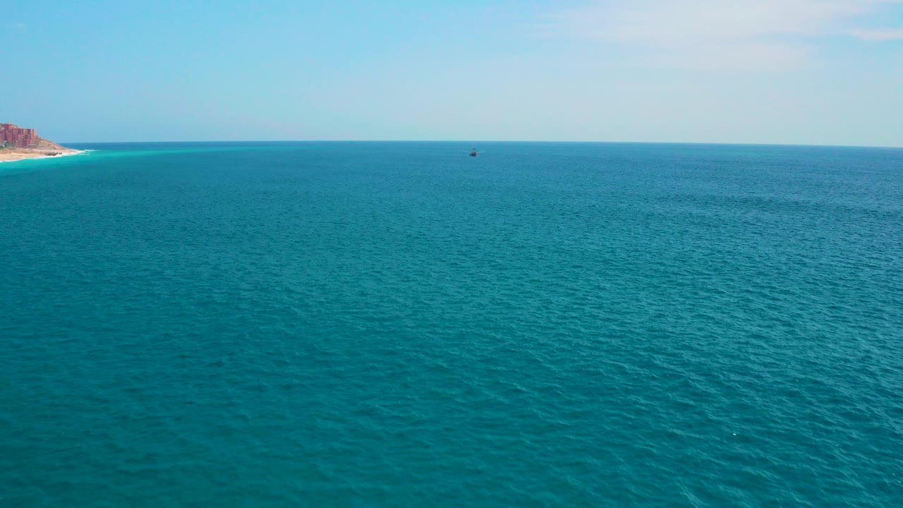 Opening frame of the Secrets Marquis Los Cabos, Mexico clip showing broad turquoise ocean, pale blue sky, a distant dark speck on the water, and no visible people.