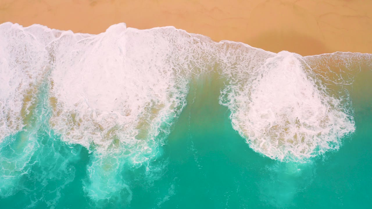 Overhead turquoise surf breaking onto tan sand.