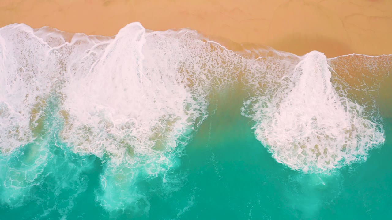 Overhead shoreline view with a dense white surf band curling over turquoise water below tan beach sand at Secrets Marquis Los Cabos, Mexico, with no visible people.