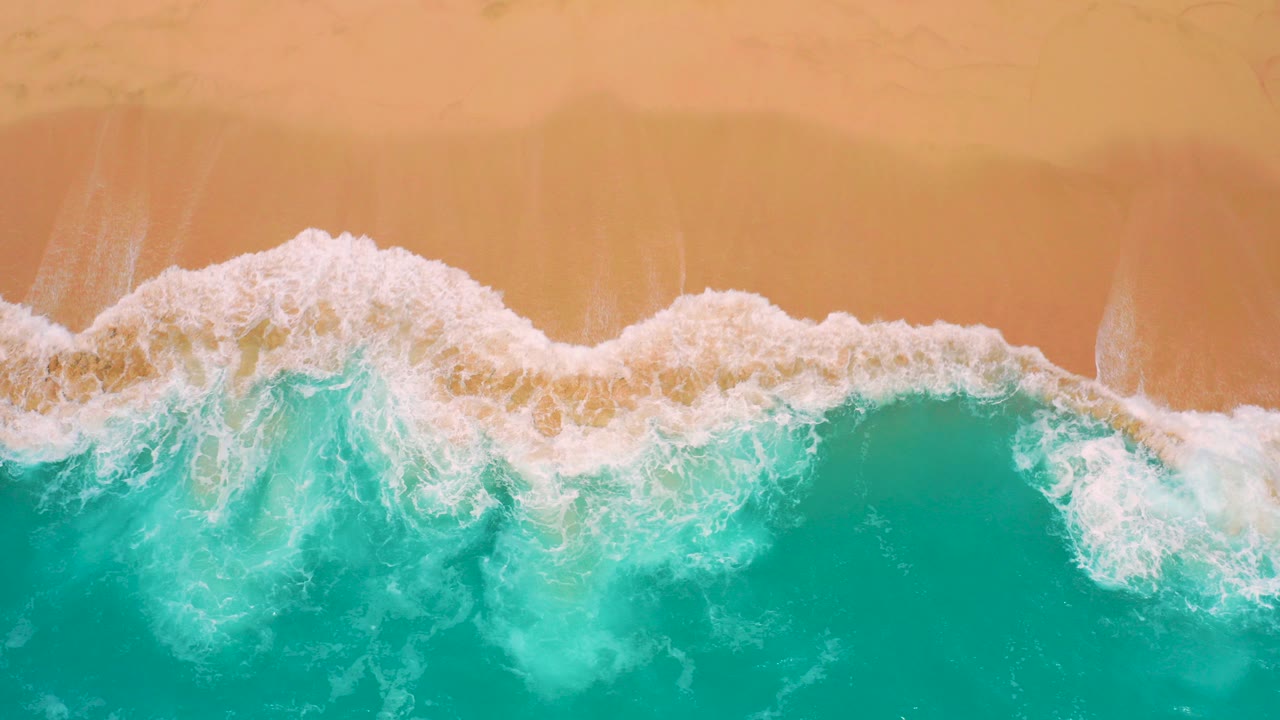 Overhead view at Secrets Marquis Los Cabos, Mexico, with turquoise water and a thin white foam line reaching golden sand, no visible people.