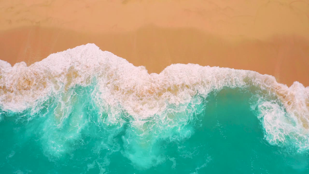 Bird's-eye shoreline view at Secrets Marquis Los Cabos, Mexico, with a wide white breaking wave curving between teal ocean and smooth golden sand, no visible people.