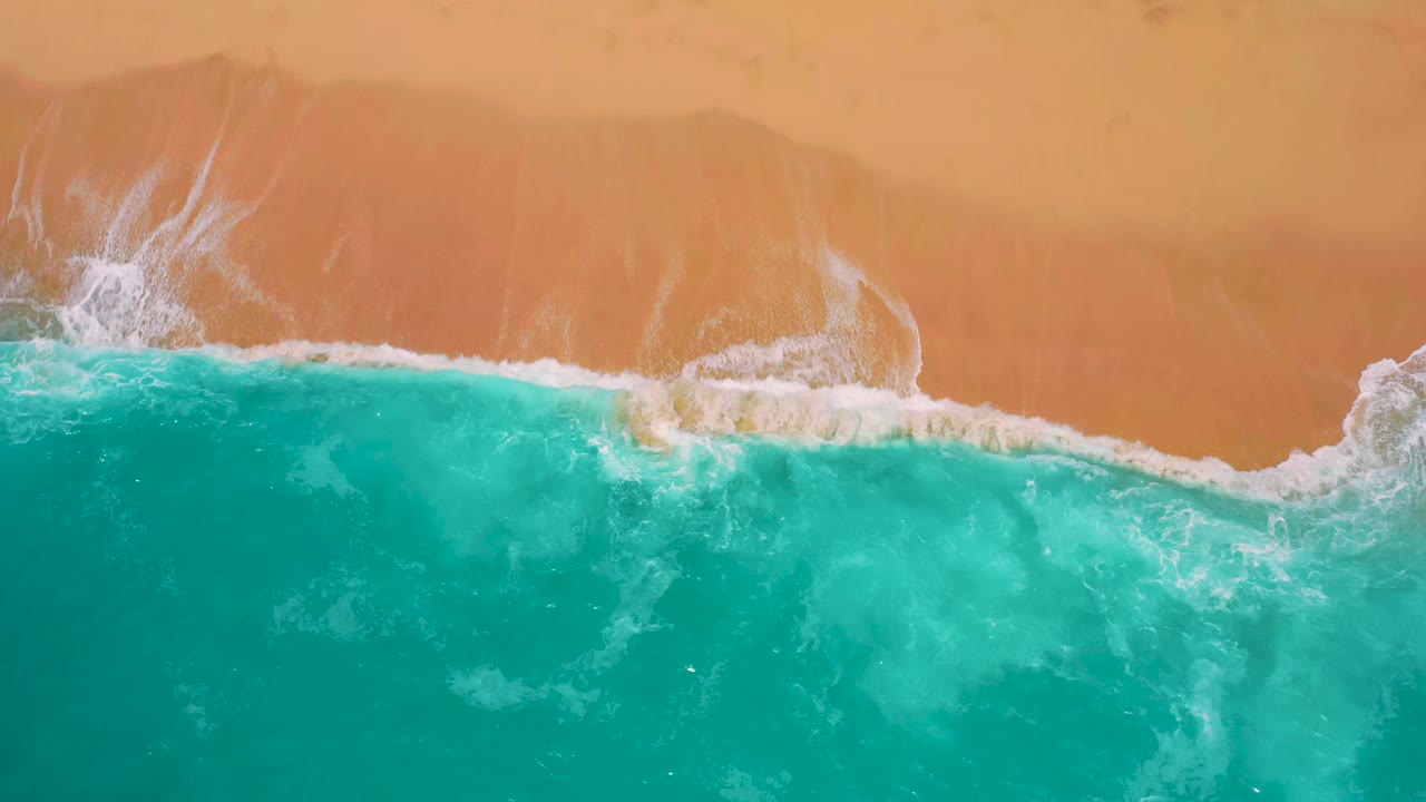 A low band of white foam runs along the red sand as clear blue-green water fills the lower frame at Secrets Marquis Los Cabos, Mexico, with no visible people.