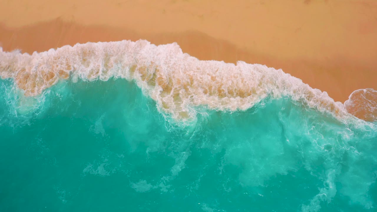 White wash spreads diagonally over shallow turquoise water and red sand at Secrets Marquis Los Cabos, Mexico, with the beach still free of visible people.