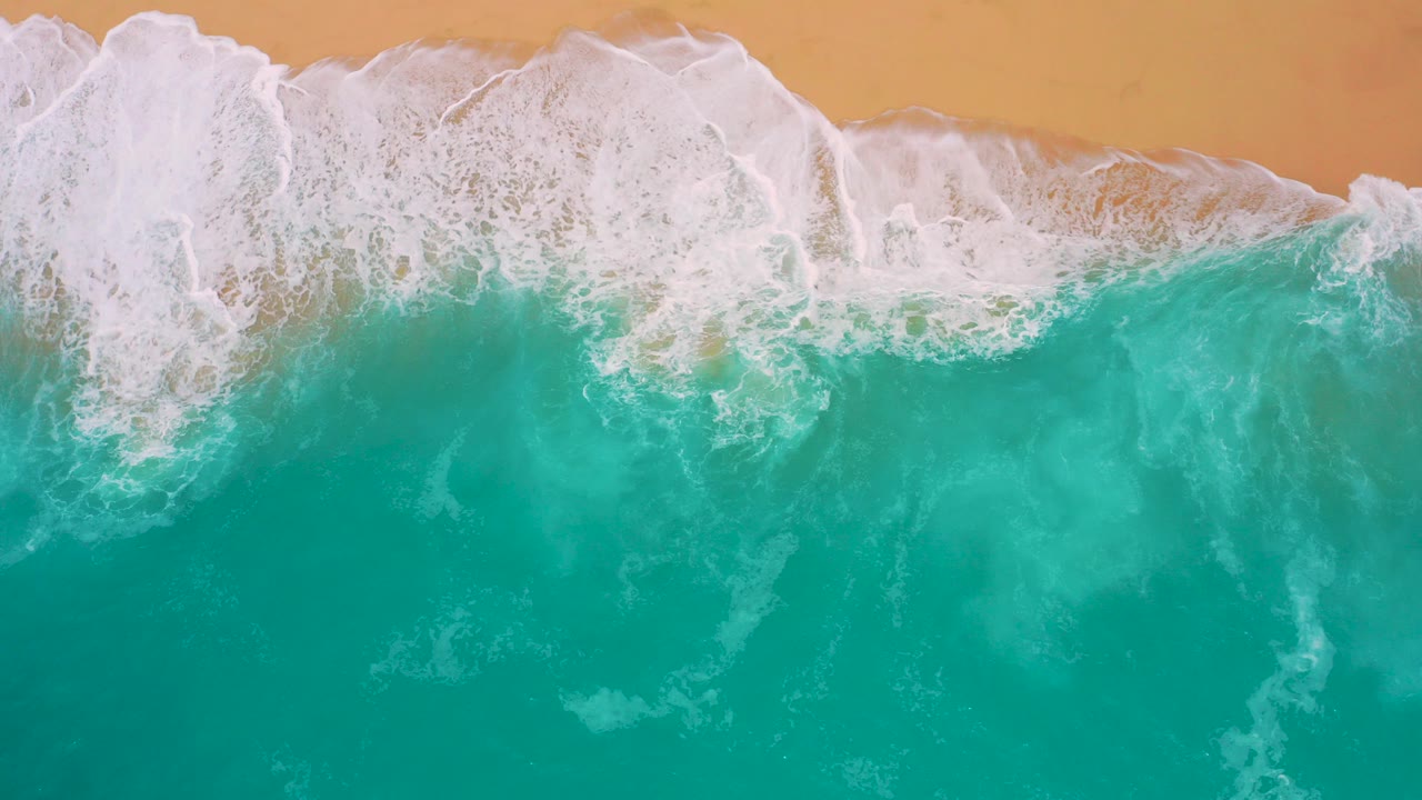 Overhead view at Secrets Marquis Los Cabos, Mexico, with turquoise water below a thick white foam line reaching tan sand and no visible people.