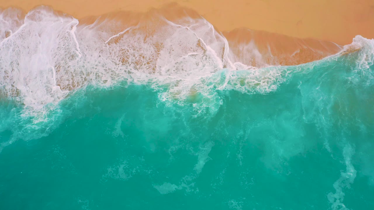 Turquoise ocean fills most of the frame while white surf curls across the top beside tan sand at Secrets Marquis Los Cabos, Mexico, with no visible people.