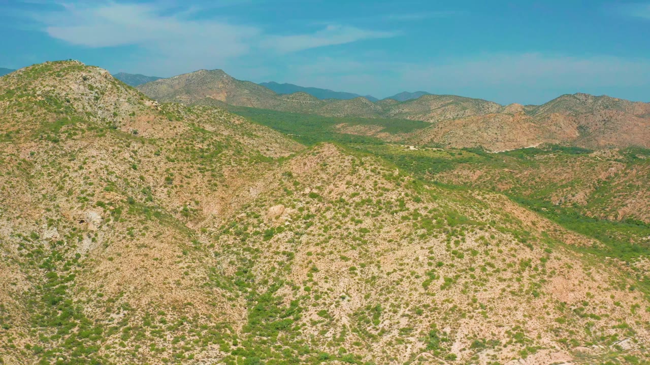 Opening aerial frame of rocky, shrub-covered hills near Secrets Marquis Los Cabos, Mexico, with distant ridges and no visible people.