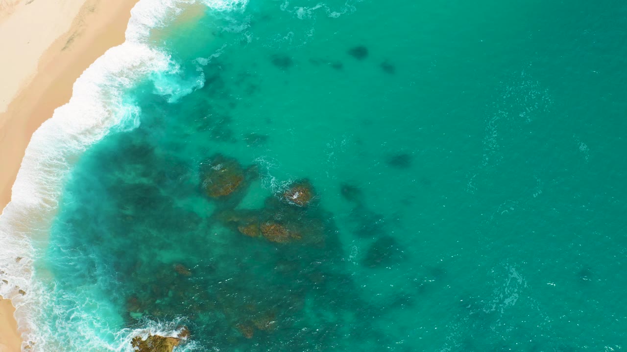 Overhead wave wash across green water with sandy beach along the left side.
