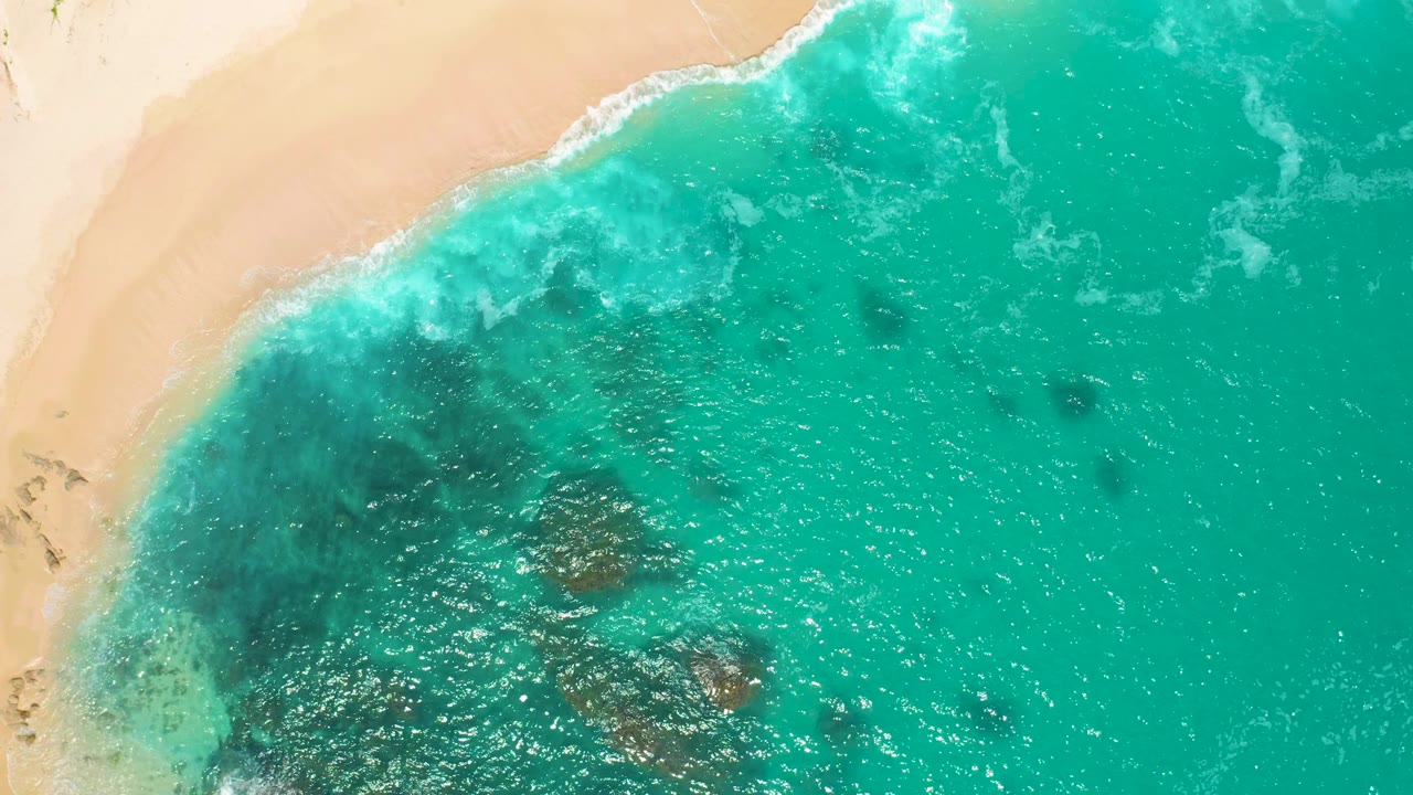 Bright overhead frame from Secrets Marquis Los Cabos, Mexico, showing shallow green surf crossing darker underwater areas near the sand, with no visible people or structures.