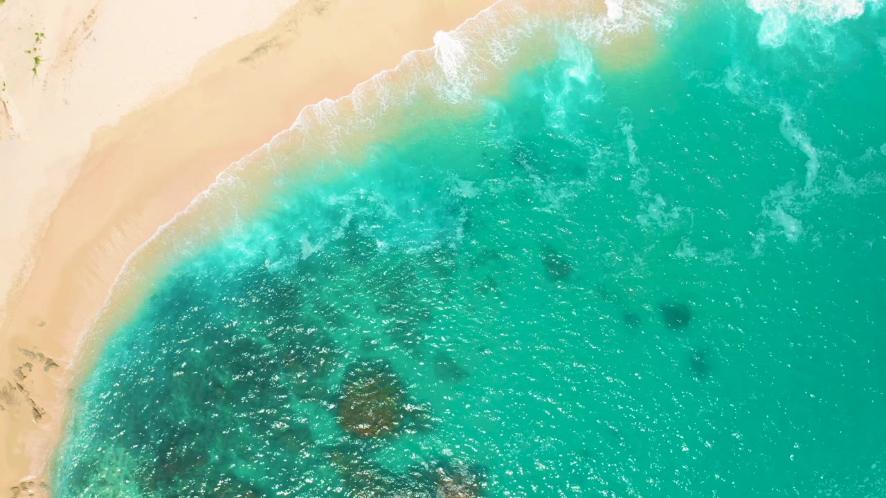 Aerial view over Secrets Marquis Los Cabos, Mexico with the sandy beach along the upper frame, white shore break, teal water, and no visible people.