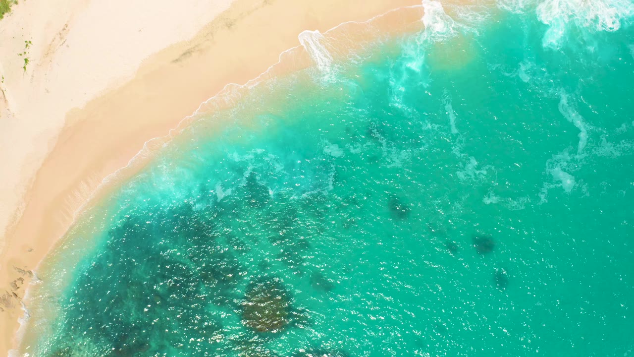 Overhead frame from Secrets Marquis Los Cabos, Mexico with pale beach on the left and top, rolling white surf, speckled teal water, and no visible people.