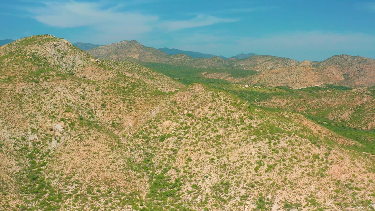 Elevated view near Secrets Marquis Los Cabos, Mexico, with shrub-dotted tan hills filling the foreground, hazy blue ridges in the distance, and no visible people.