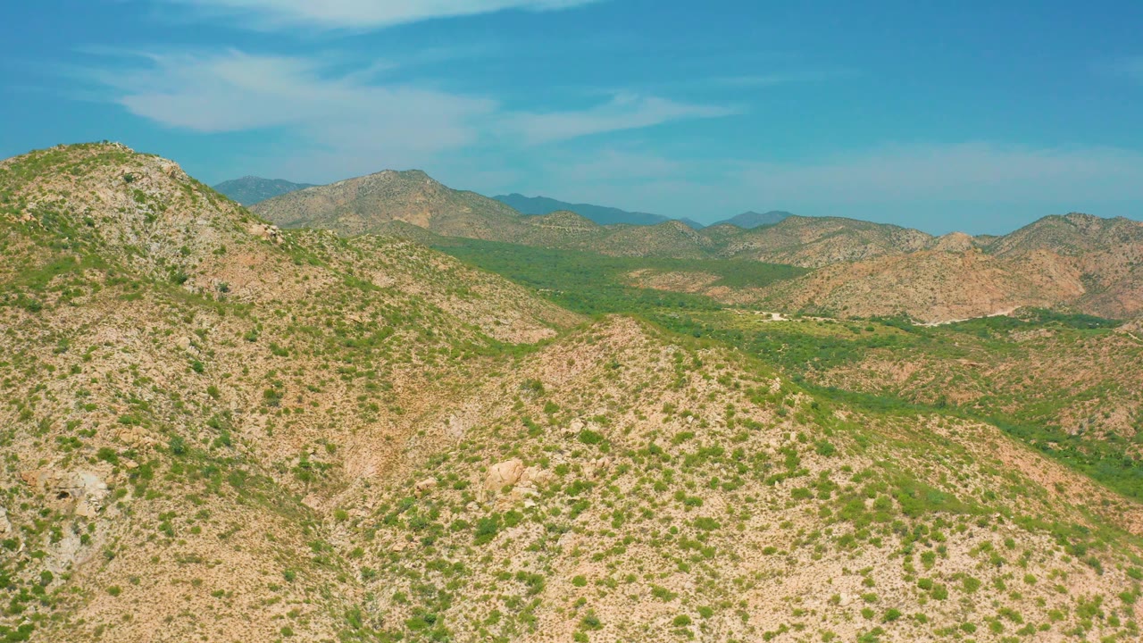 Opening view of rocky tan hills and green desert vegetation near Secrets Marquis Los Cabos, Mexico, with no visible people.