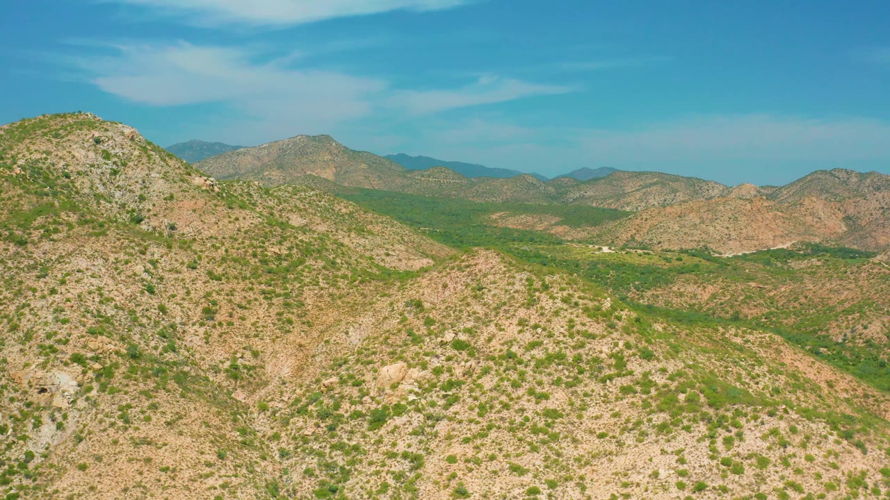 Rocky hills frame a green desert valley beneath a clear blue sky in the Secrets Marquis Los Cabos, Mexico clip, with no visible people.