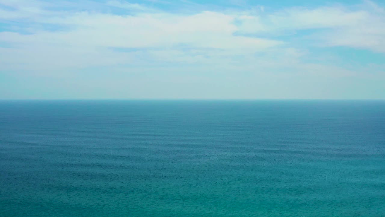 Turquoise water in the foreground shifts into deeper blue toward the horizon at Secrets Marquis Los Cabos, Mexico, with broken cloud cover and no visible people.