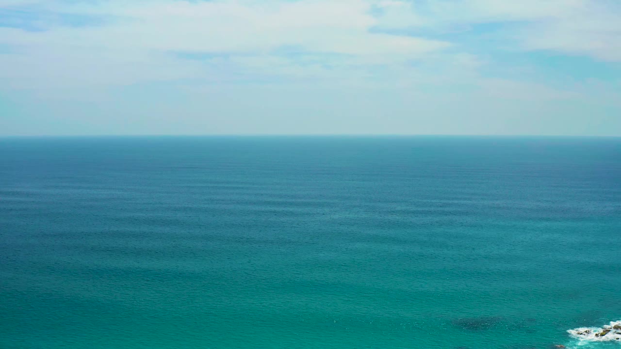 Aerial ocean view at Secrets Marquis Los Cabos, Mexico, with turquoise water, a small white wave break on rocks near the lower right, and no visible people.