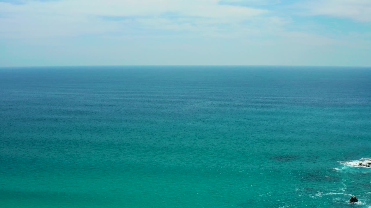 At Secrets Marquis Los Cabos, Mexico, a wide elevated view looks over blue green ocean toward a straight horizon, with small rocks and white surf low in the frame and no visible people.