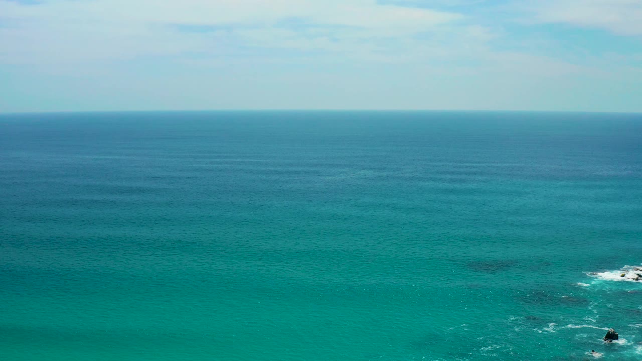 At Secrets Marquis Los Cabos, Mexico, a broad turquoise ocean view reaches to the horizon, with a white surf patch and dark rocks near the lower right edge and no visible people.
