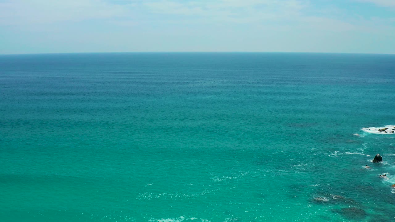 Wide coastal water view from Secrets Marquis Los Cabos, Mexico, with turquoise shallows, darker water bands, rock outcrops toward the right edge, white foam, and no visible people.