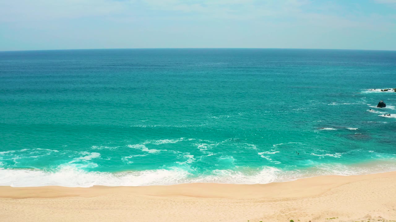 At three seconds, the Secrets Marquis Los Cabos shoreline shows layered white surf crossing shallow turquoise water toward pale sand, with no visible people.