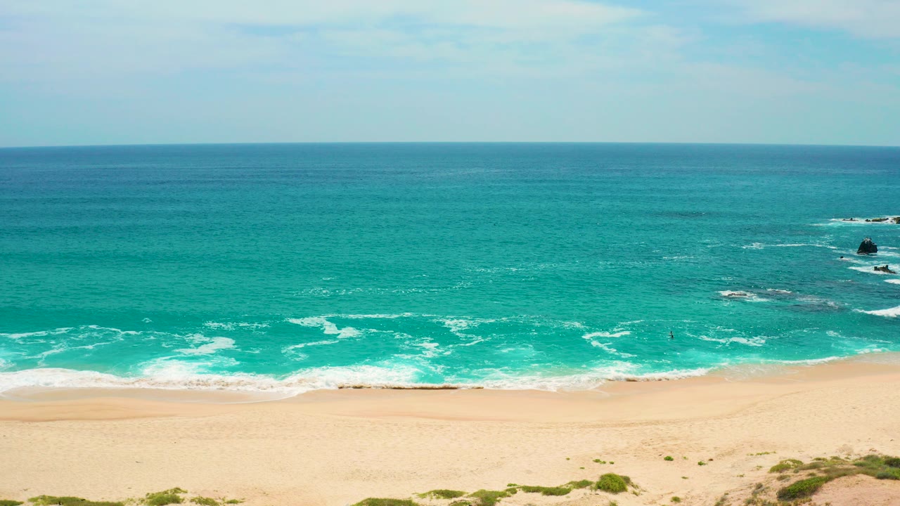 Turquoise ocean and sandy beach seen above dunes