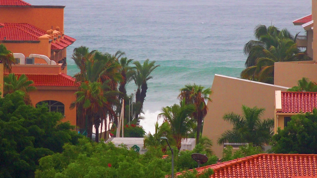 San Jose Del Cabo vacation rental exteriors with red tile roofs, palms, green foliage, pale ocean water, and no visible people at the opening frame.