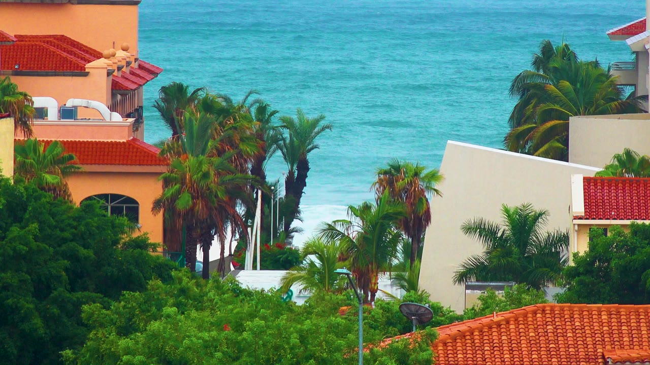 San Jose del Cabo coastal buildings with red tile roofs and palms in front of turquoise water, no visible people.