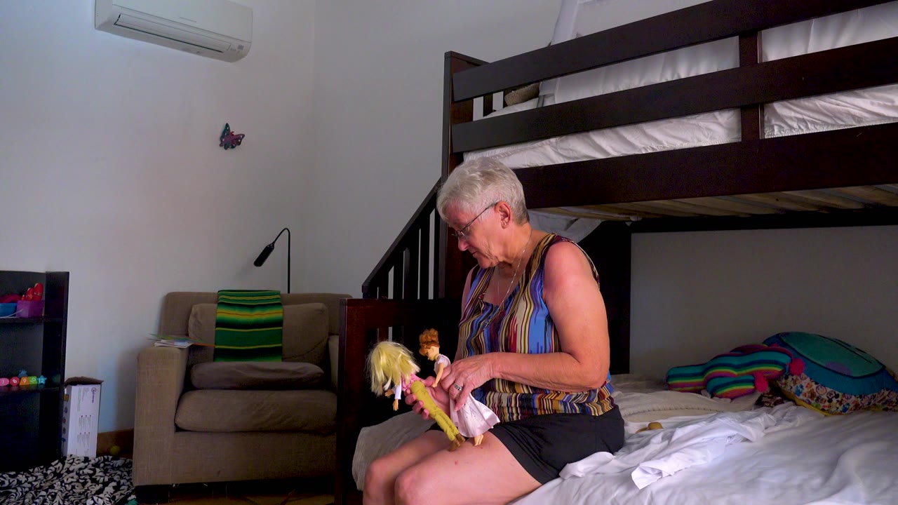 Woman looking down while handling dolls on a bed.